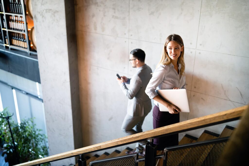 Two people with smartphones and laptops on a staircase