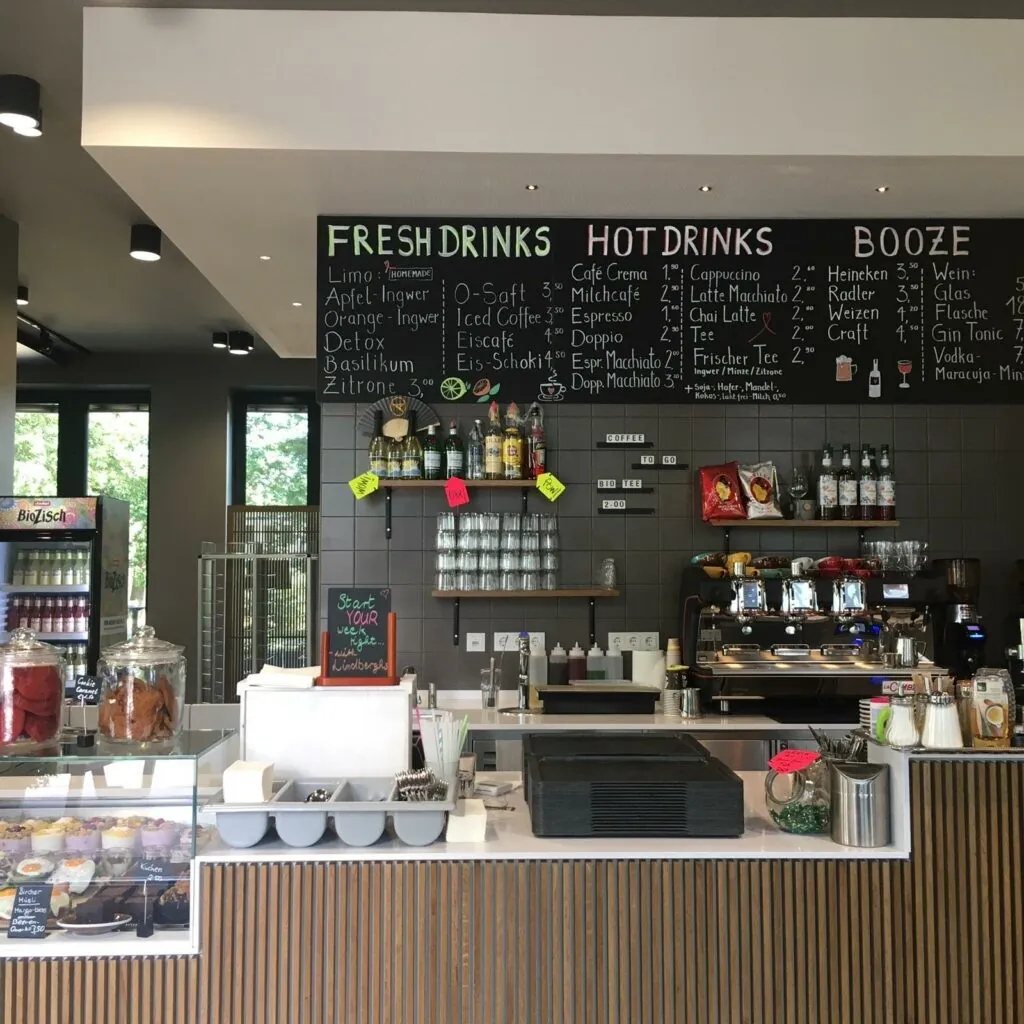 Theke eines Cafés mit Kreidetafel für Getränke, Kuchenvitrine und Espressomaschine.