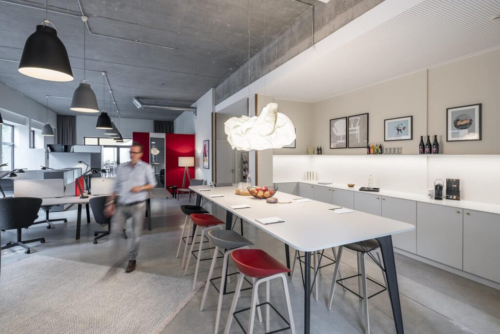 Long bar table with bar stools in front of the tea kitchen, above a large paper lamp, with the work stations in the background