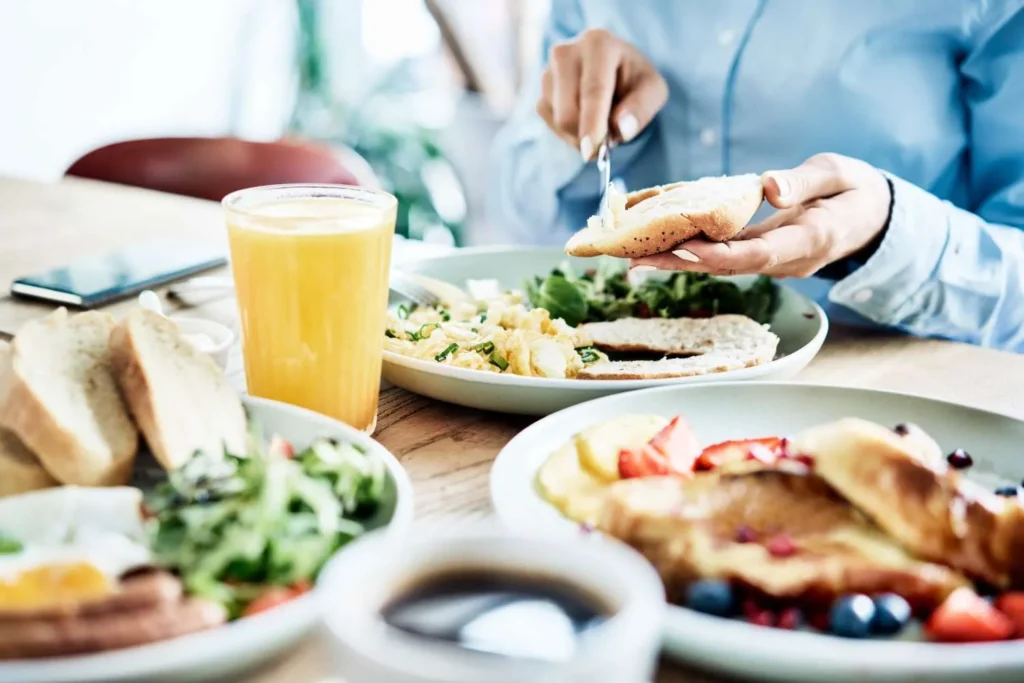 Ein Frühstückstisch mit Orangensaft, Rührei, Brot, Salat und Pfannkuchen mit Beeren.