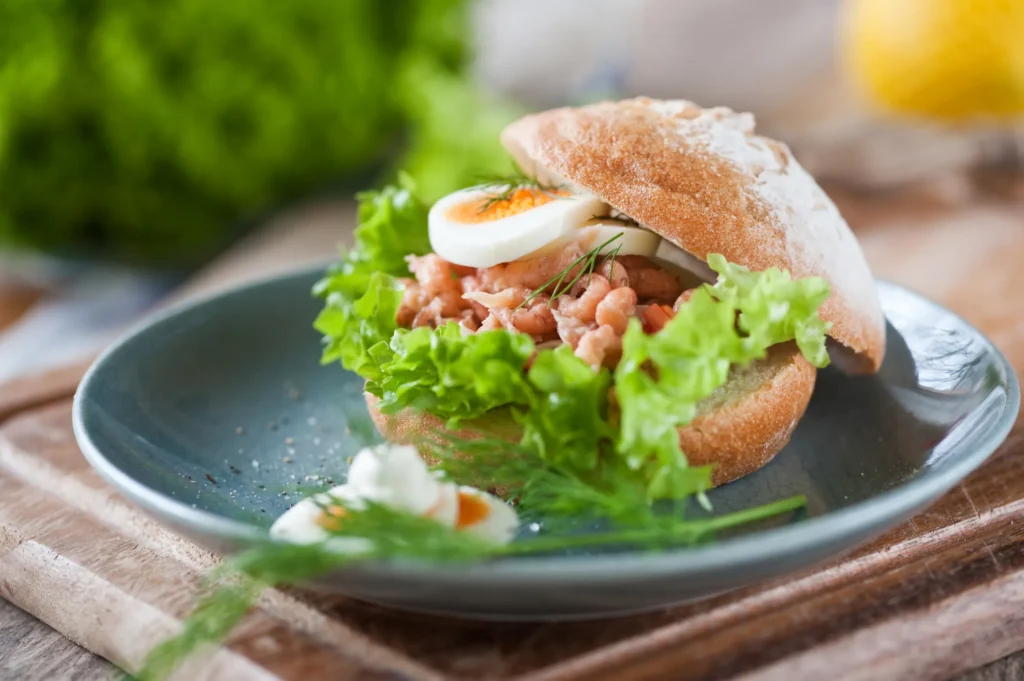 Fischbrötchen mit Nordseekrabben, Ei, Salat und Dill auf einem blaugrauen Teller.
