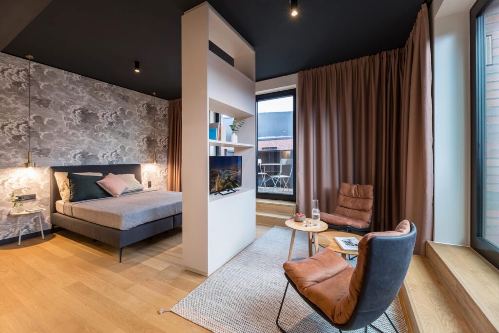 Apartment M in ipartment Hamburg with a bed, a room divider shelf and a armchair by the window
