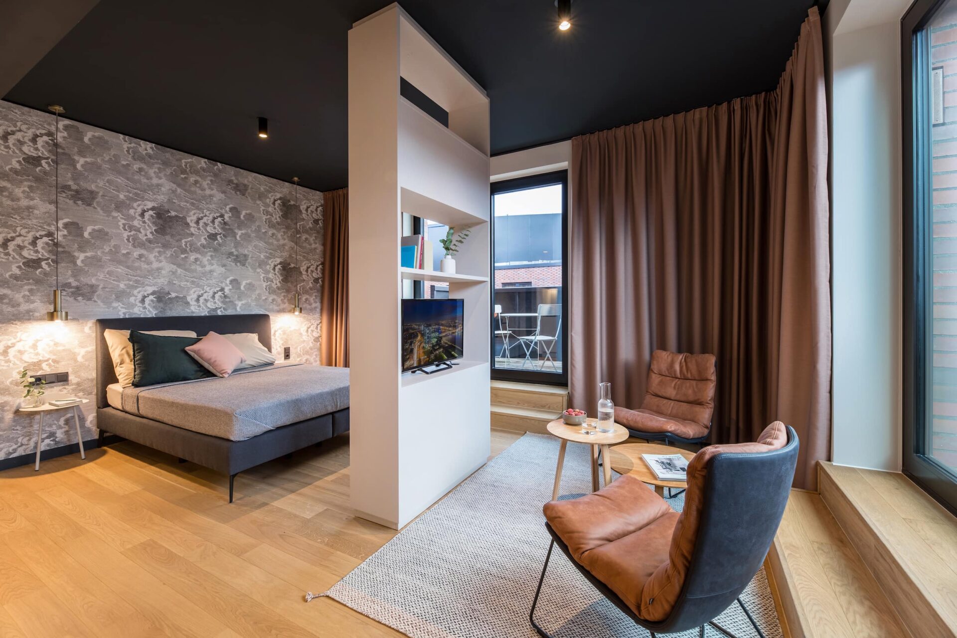 Apartment M im ipartment Hamburg mit Bett, Raumteiler-Regal und Sessel am Fenster