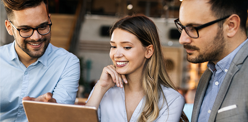 Three colleagues are looking at a laptop together with a smile