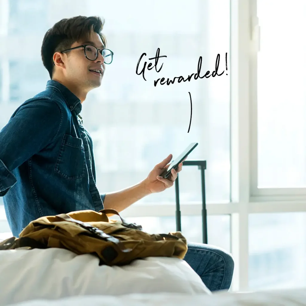 Man with mobile phone next to a yellow suitcase at the window of an apartment, lettering „Get rewarded!“ and Best Western logo