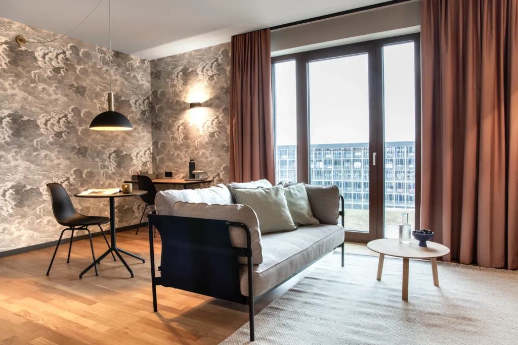 Wohnbereich mit Sofa, Couchtisch, Wolkentapete und bodentiefen Fenstern im Apartment L, ipartment Berlin Airport