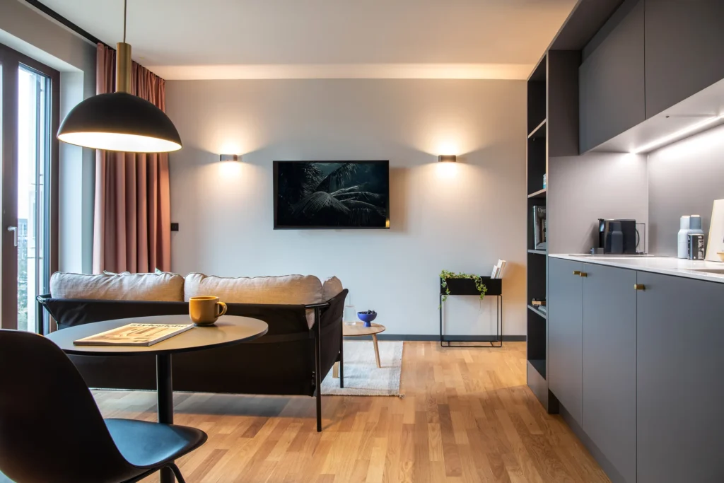 Living area with sofa, round dining table and grey kitchen unit in Apartment L, ipartment Berlin Airport