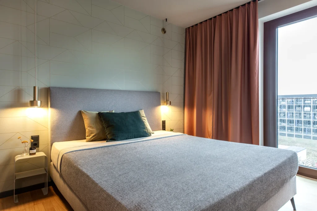 Double bed with grey blanket, wall lights and window with curtain in Apartment L, ipartment Berlin Airport