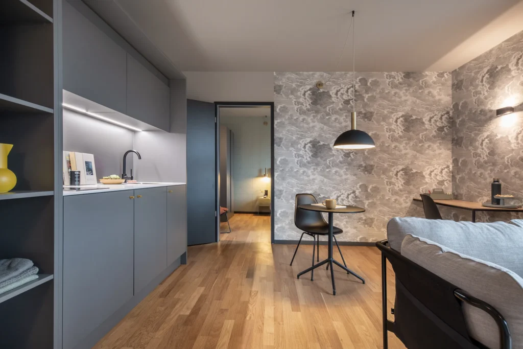 Kitchenette and dining table in front of the wallpaper with a view of the bedroom in Apartment L, ipartment Berlin Airport