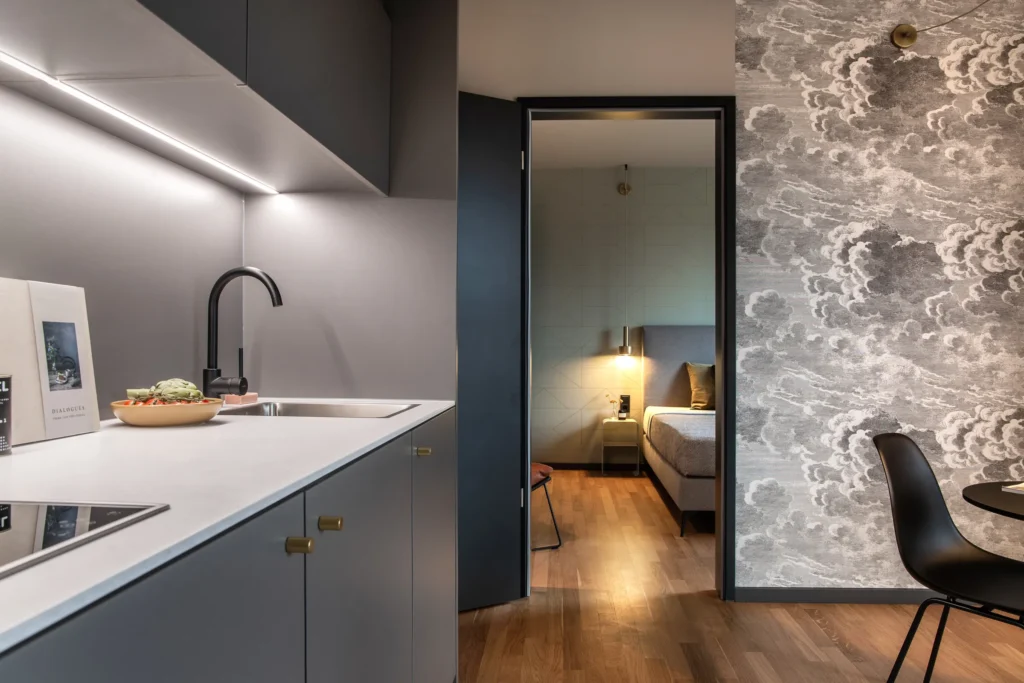 Kitchenette with sink and access to the bedroom next to the wallpaper mural in apartment L, ipartment Berlin Airport
