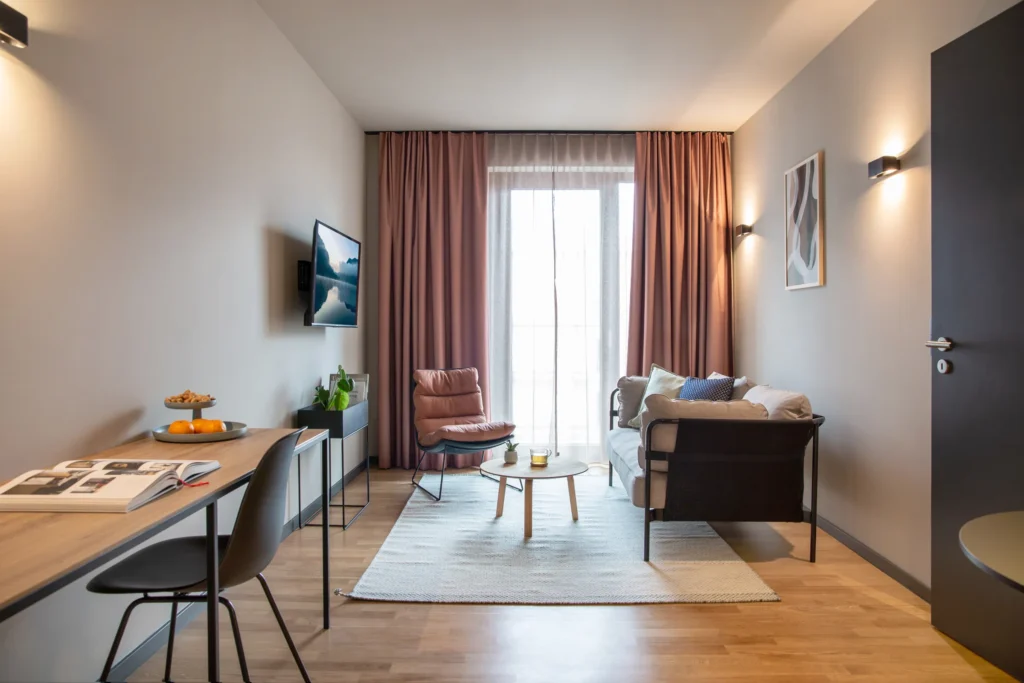 Living area with desk, leather armchair, sofa and TV in Apartment M, ipartment Berlin Airport