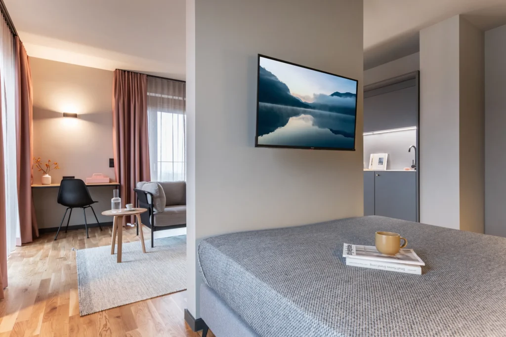 View from the bed towards the TV, desk and armchair by the window in Apartment M, ipartment Berlin Airport