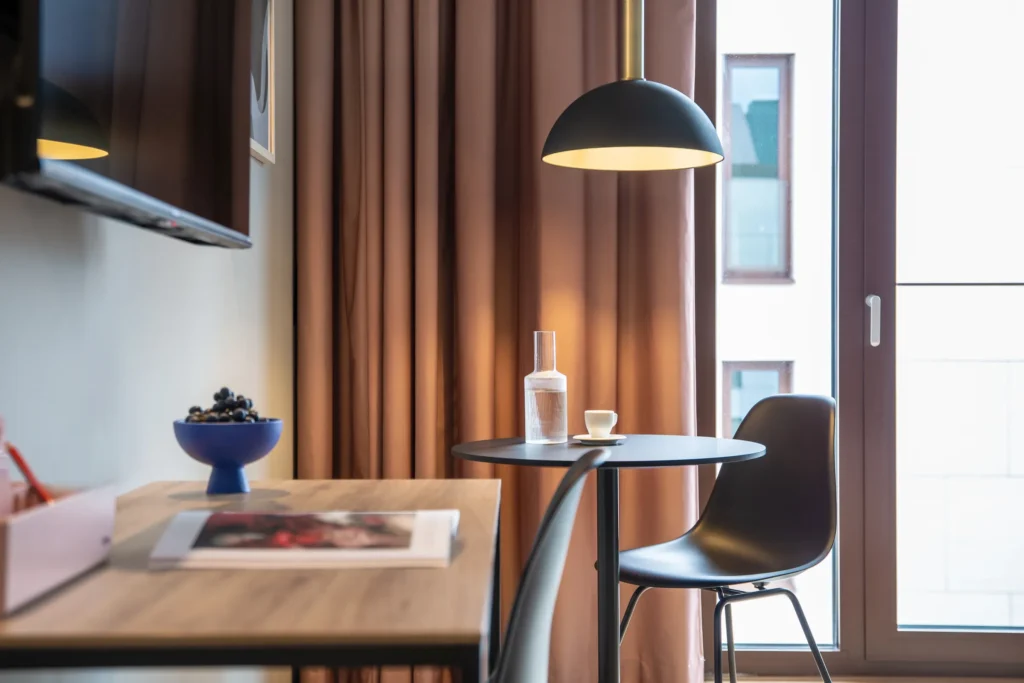 Round dining table with chair and pendant light in front of a window with a curtain in Apartment S, ipartment Berlin Airport