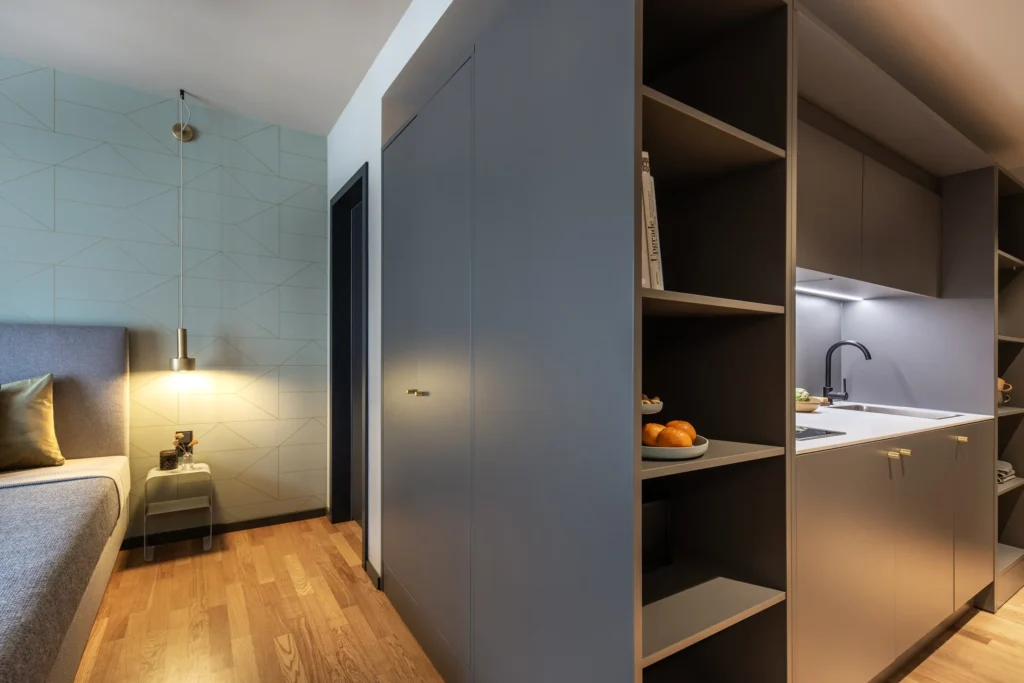 Bed, built-in cabinet, shelf and kitchenette with black faucet in Apartment S, ipartment Berlin Airport