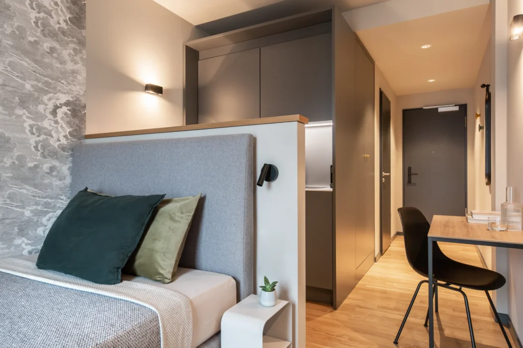 Bed with a cloud wallpaper on the headboard, entrance hallway and work desk in the XS apartment, ipartment Berlin Airport