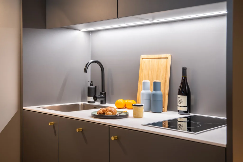 Kitchenette with black faucet, stove, croissant and red wine in the XS apartment, ipartment Berlin Airport