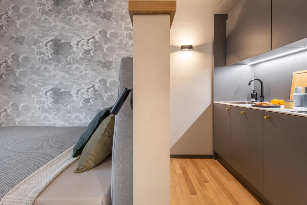 Bed with a wall mural and kitchenette with a wall lamp in the XS apartment, ipartment Berlin Airport