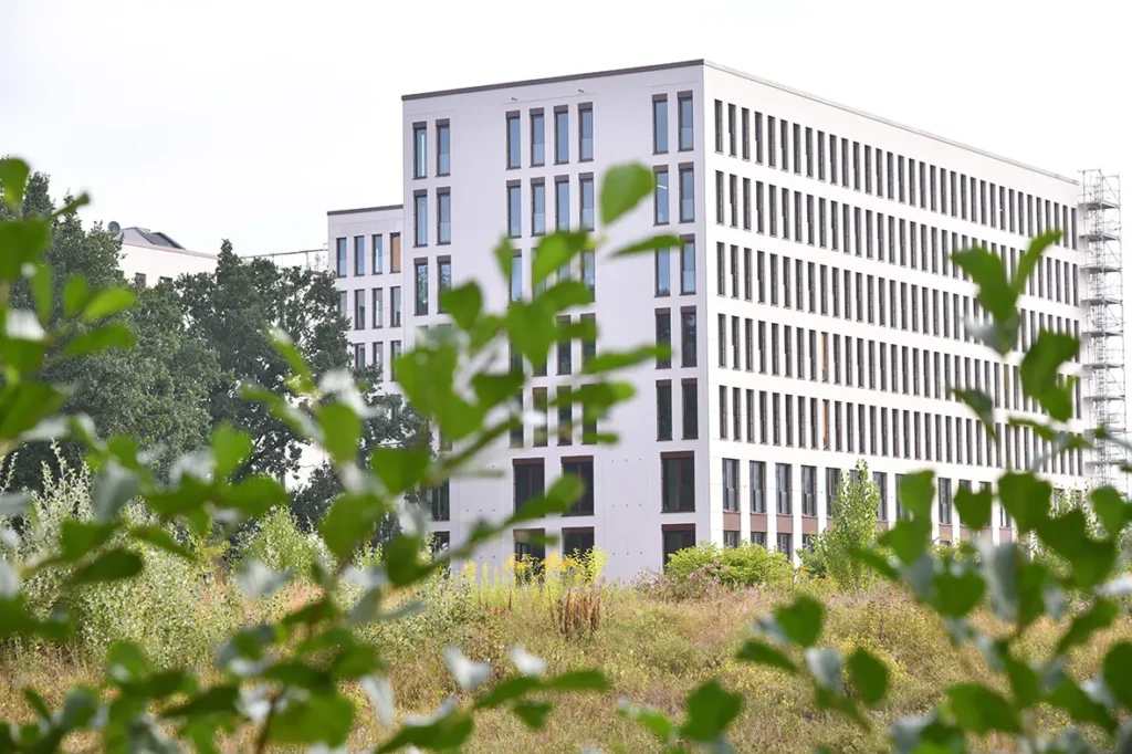 Bright building with regular window spacing behind greenery, ipartment Berlin Airport at BER airport