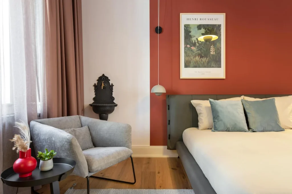 Double bed in front of a red-and-brown wall, armchair with side table and parquet floor in the Medium apartment, ipartment Berlin Kurfürstendamm