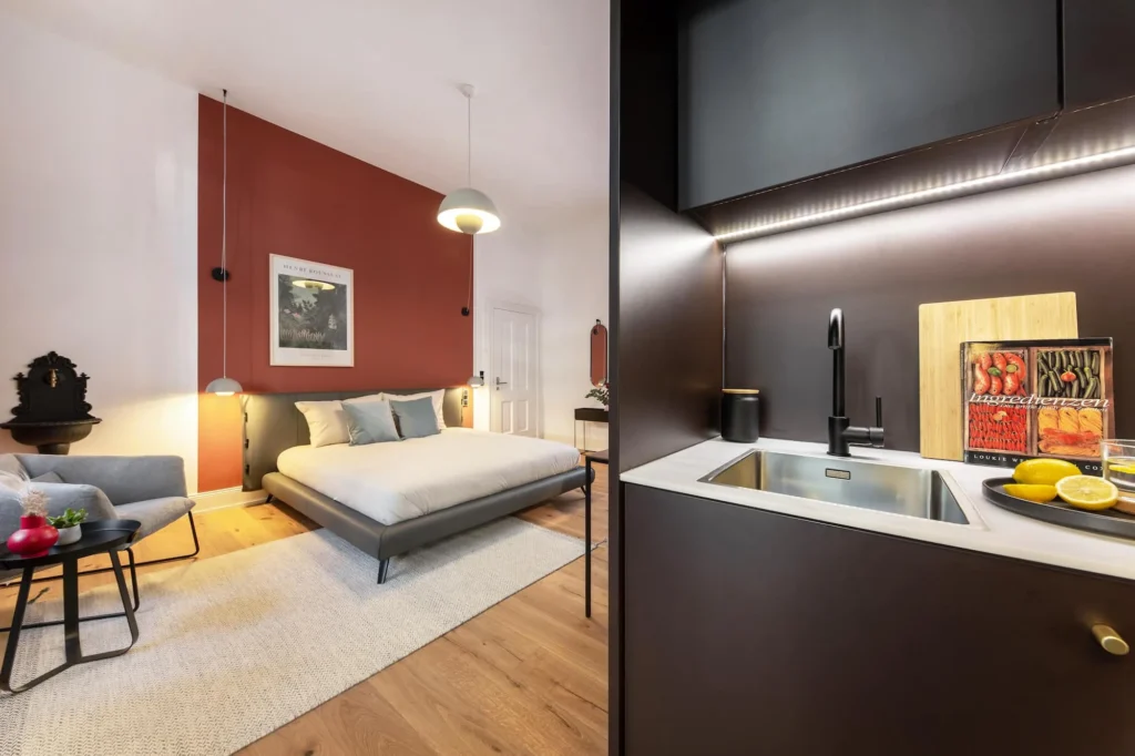 Sleeping area with double bed and dark kitchen area with sink in the Medium apartment, ipartment Berlin Kurfürstendamm