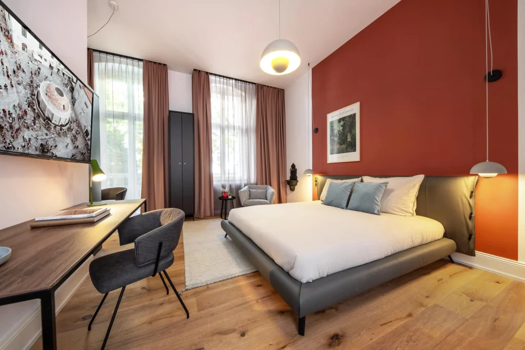 Double bed with desk, TV and high windows with curtains in the Medium apartment, ipartment Berlin Kurfürstendamm