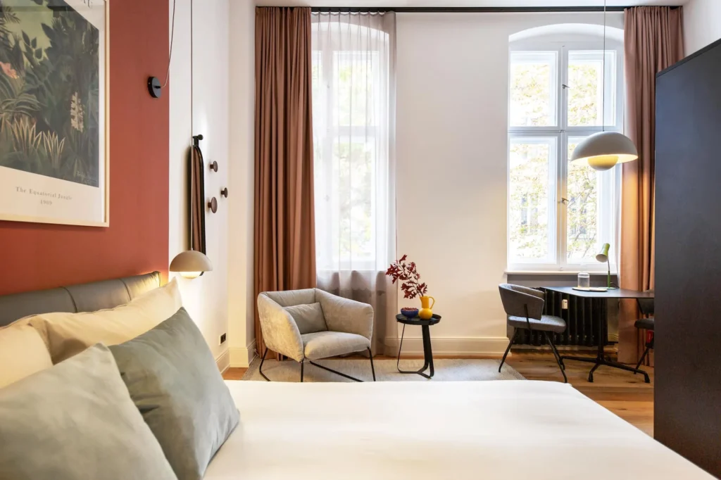 Großes Bett, Sessel und Essplatz vor hohen Altbaufenstern mit Vorhängen im Apartment Smart, ipartment Berlin Kurfürstendamm