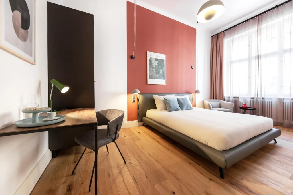 Sleeping area with double bed, desk and high old-style windows in the Smart apartment, ipartment Berlin Kurfürstendamm