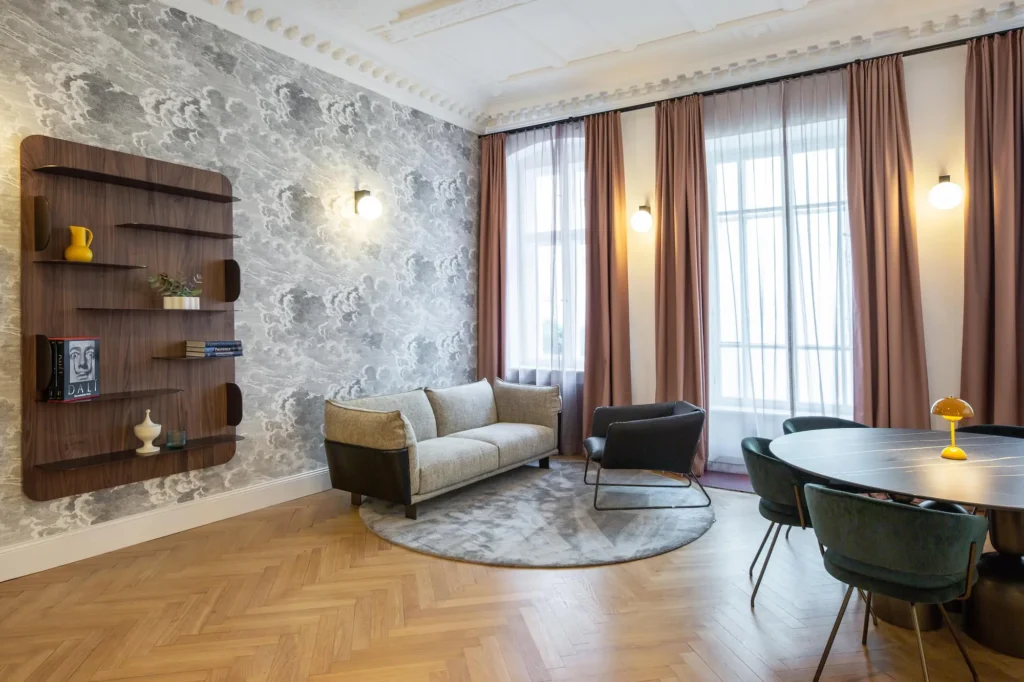 Lounge with sofa, armchair, wall shelf and dining table under stucco ceiling with herringbone parquet, ipartment Berlin Kurfürstendamm