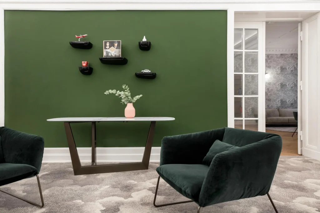Lounge with green wall, dark green chairs and table with vase, ipartment Berlin Kurfürstendamm