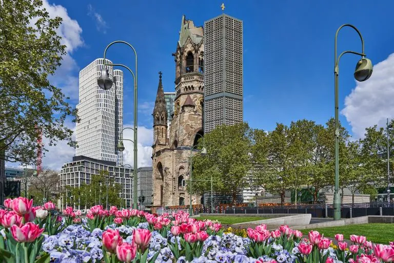 Caius-Wilhelm Memorial Church between high-rise buildings, in front of it a flowerbed with tulips and primroses, Berlin