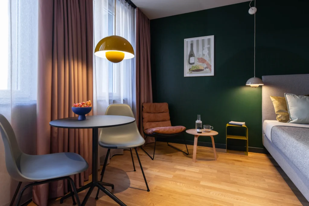 Sitting area with table and chairs in front of a dark green wall and a bed in apartment S, Berlin Mitte
