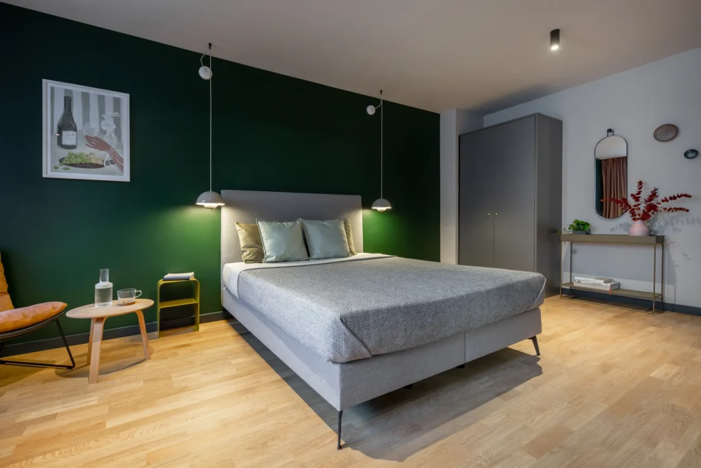 Double bed in front of a dark green wall with a wardrobe and a mirror in Apartment S, Berlin Mitte