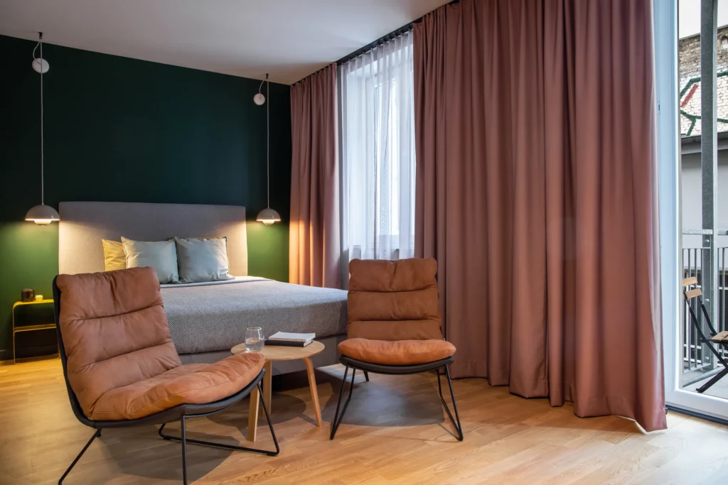 Bed with armchairs and side table in front of the curtain and balcony door in Apartment S+, ipartment Berlin Mitte