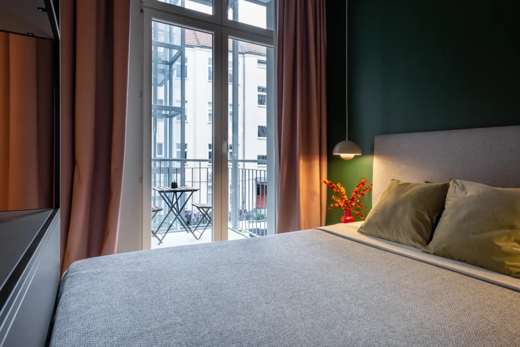 Bed in dark green wall with a view through the balcony door to the balcony in the S+ apartment in the Berlin Mitte district