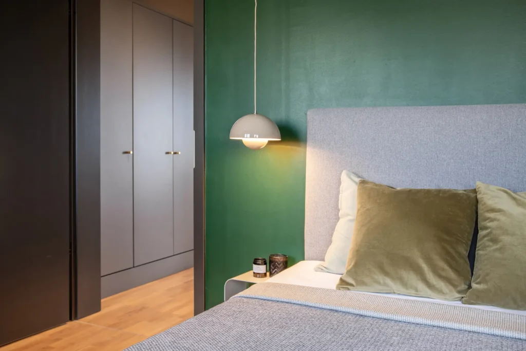 Bett mit Kleiderschrank, grüner Wand und Pendelleuchte im Apartment XL, ipartment Berlin Mitte