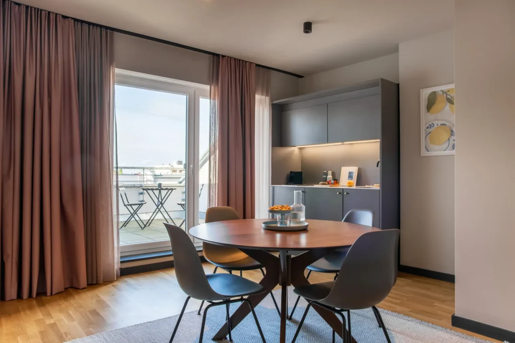 Dining table with chairs, kitchenette and balcony door with a view of the roofs in the XL apartment, ipartment Berlin Mitte