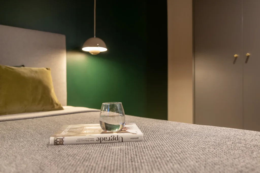 Close-up of the bed with a green wall, pendant light and wardrobe in the XS apartment, ipartment Berlin Mitte