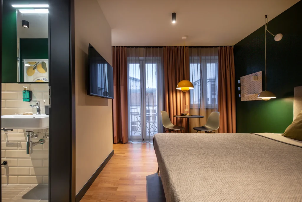 Bett, Sitzecke am bodentiefen Fenster zum Balkon und Blick ins Bad im Apartment XS+, ipartment Berlin Mitte