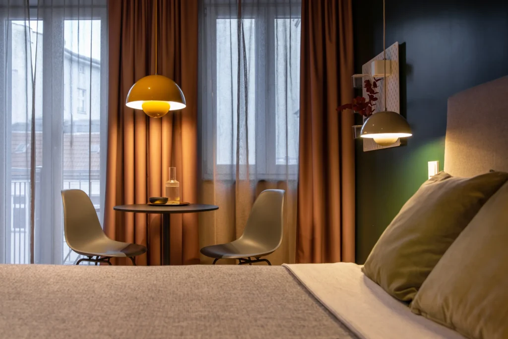 Round table with two chairs in front of floor-to-ceiling windows; bed in the foreground in the XS+ apartment in the ipartment Berlin Mitte