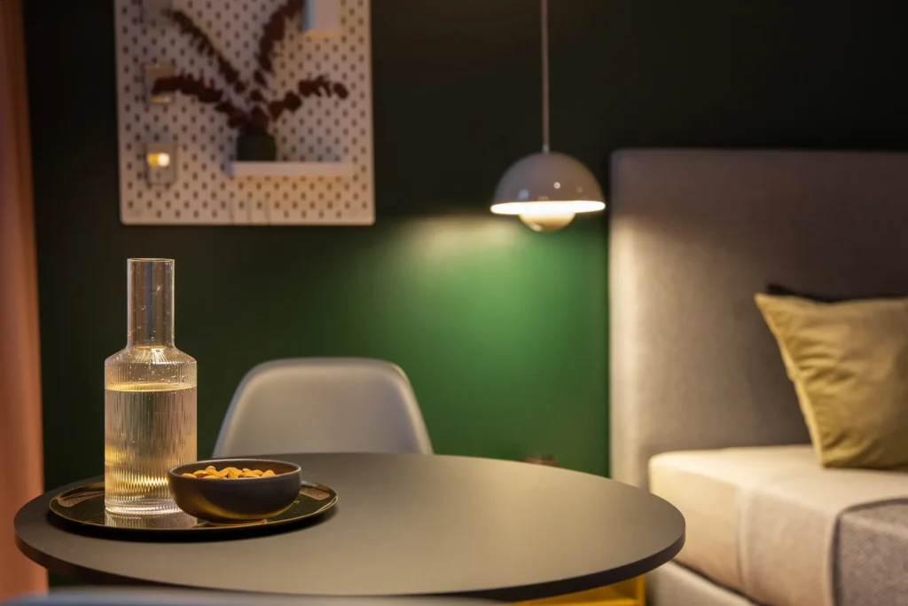 Jar and bowl on the table in front of the bed with a green wall in the XS+ apartment, ipartment Berlin Mitte