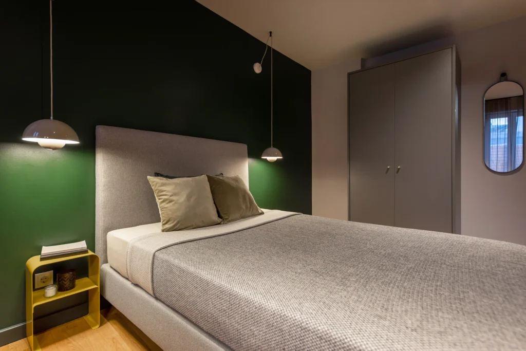 Single bed with green wall, pendant lights and wardrobe in the XS+ apartment, ipartment Berlin Mitte