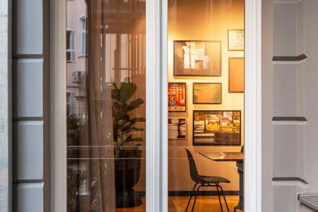 View through a window into the evening-lit lounge with framed pictures, ipartment Berlin Mitte