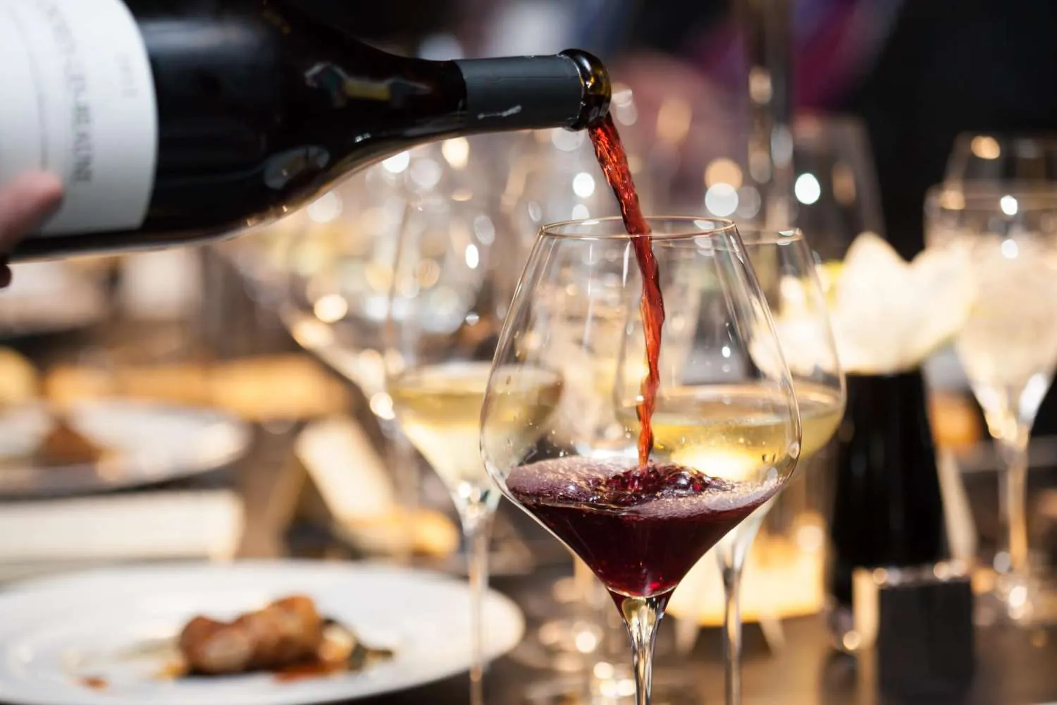 Rotwein wird aus der Flasche in ein Weinglas auf einem gedeckten Tisch gegossen.