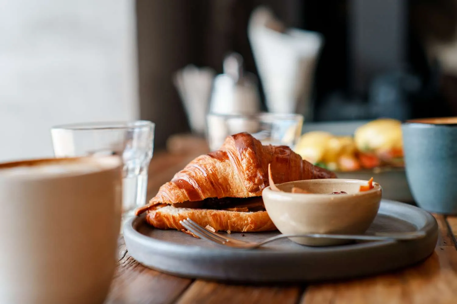 Ein Croissant mit Belag und ein Milchkaffee stehen auf einem Holztisch im Café.
