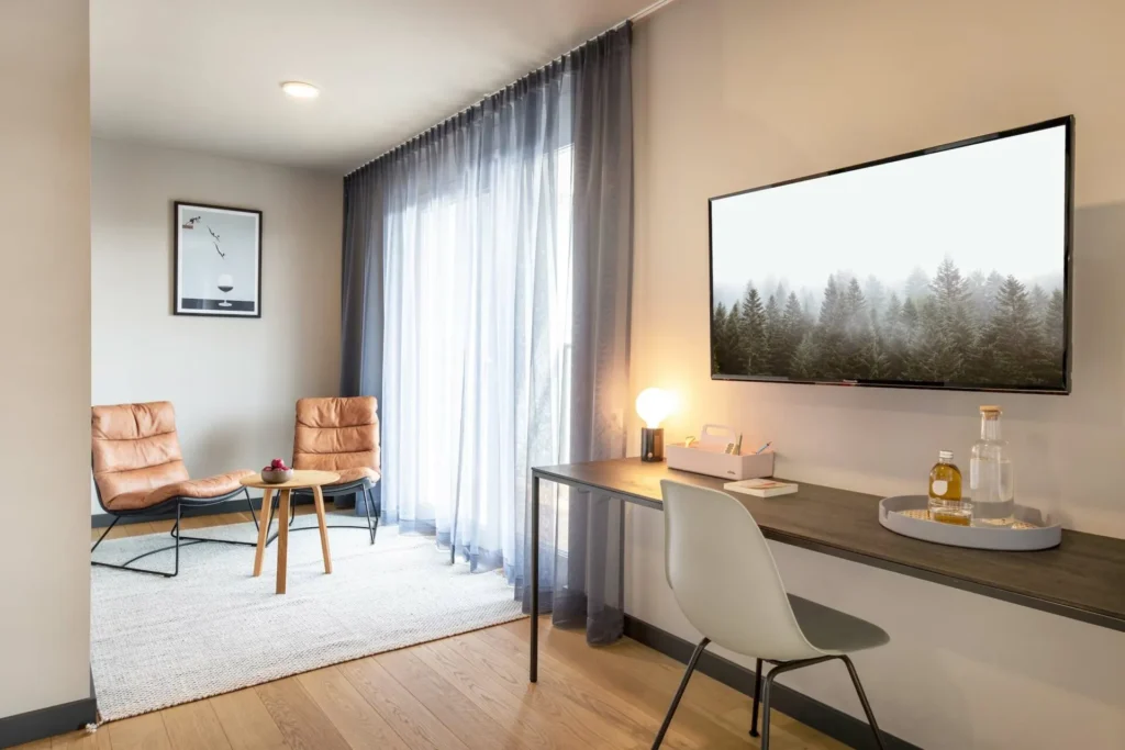Living area with desk, wall-mounted TV and two armchairs in front of the window in the Luxury apartment, ipartment Böblingen-Sindelfingen