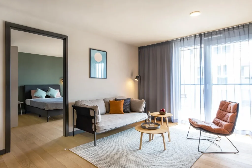 Living area with sofa, armchair and coffee table; through the door to the sleeping area in the Medium apartment, ipartment Böblingen-Sindelfingen