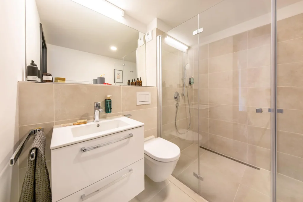 Bathroom with sink, toilet and glass shower in beige tiles in the Medium apartment, ipartment Böblingen-Sindelfingen