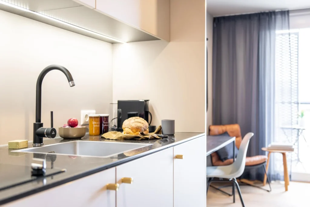 Kitchenette with sink and coffee machine, next to it a chair by the window in the Xtra Smart apartment, ipartment Böblingen-Sindelfingen