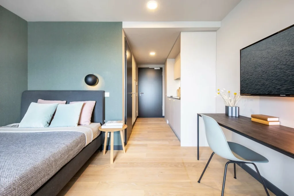View from the bed through the hallway to the front door, with a desk and kitchenette in the Xtra Smart apartment, ipartment Böblingen-Sindelfingen