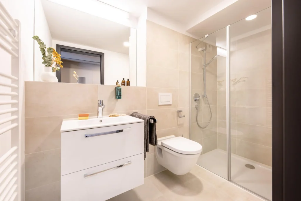 Bathroom with sink, toilet and glass shower in beige tiles in the Xtra Smart apartment, ipartment Böblingen-Sindelfingen